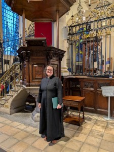 Image of Rev Canon Bryony Taylor standing next to the pulpit at Derby Cathedral